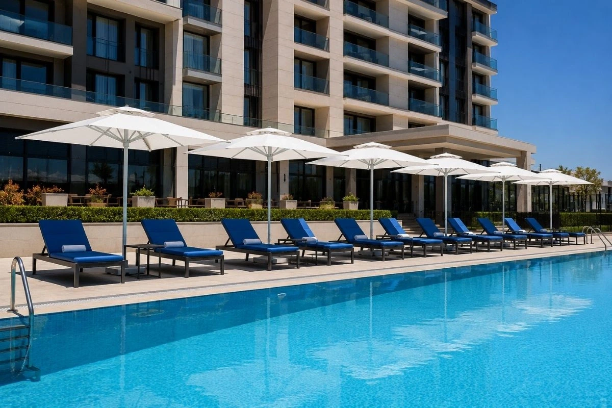 Ankara Havuz Şemsiyesi | Otel Havuzu ve Şezlong Gölgelendirme Sistemi Ankara otel havuzunda beyaz şemsiyeler ve mavi minderli şezlonglarla modern havuz gölgelendirme sistemi